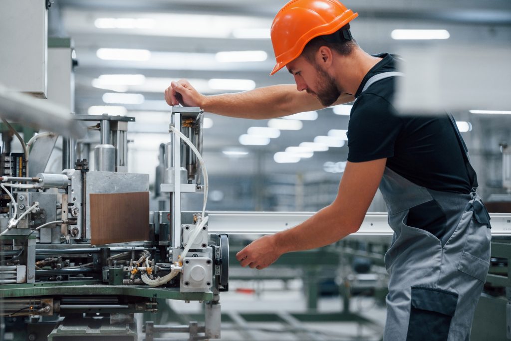 Operator of machine. Industrial worker indoors in factory. Young technician with orange hard hat